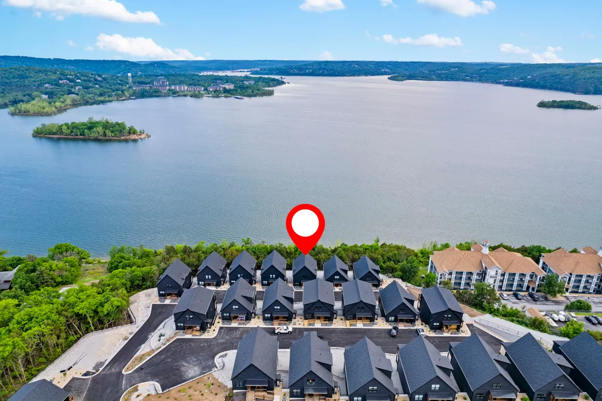 A sweeping exterior view of the lake framed by lush greenery, with a cluster of upscale houses nestled along the shoreline. The landscape exudes tranquility and showcases the property's prime lakeside location, offering a clear sense of natural beauty and serene surroundings ideal for team retreats and outdoor activities.