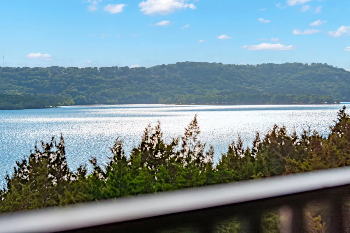 An expansive view of the lake with distant hills, blue sky, and trees in the foreground. The inviting natural scenery hints at endless outdoor opportunities like boating, fishing, hiking, and picnicking.