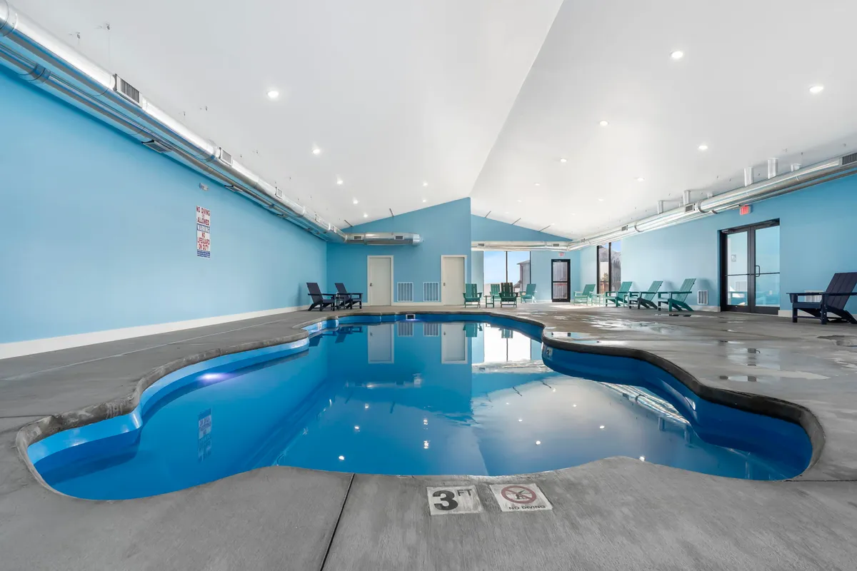 This interior shot displays an indoor swimming pool area with lounge chairs and expansive windows, creating a leisurely and social environment ideal for relaxation or group fun no matter the season.