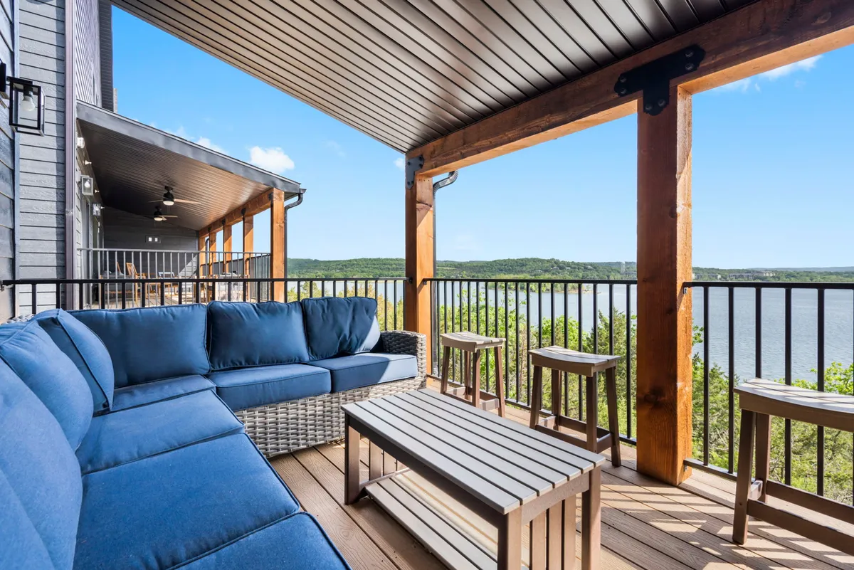 A welcoming deck scene featuring a blue sectional sofa and wooden coffee table, with an unobstructed view of the lake just beyond. The space is set up for relaxation and entertaining, offering an inviting atmosphere for family gatherings at sunset or stargazing nights.