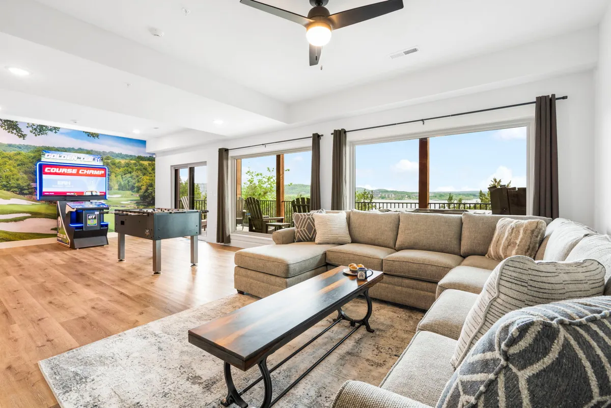A spacious game room featuring a large sectional sofa, a foosball table, a coffee table, and expansive windows with scenic views. The room is designed for both relaxation and entertainment, accommodating group gatherings for games, movies, or socializing.