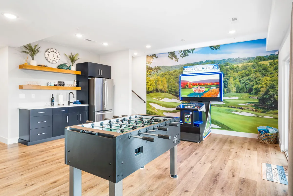 A lively recreation room featuring a foosball table, kitchenette, digital gaming station, and a striking wall mural of a golf course, showcasing spaces for fun, games, social gatherings, and easy access to refreshments.