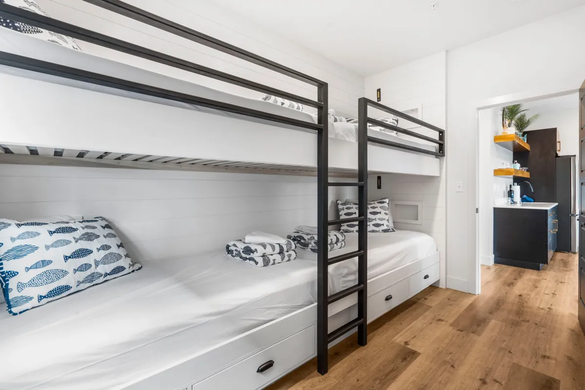 A cheerful bunk room with sturdy wooden bunk beds, playful fish-patterned pillows, and a cozy wooden floor. The space feels welcoming and fun, suggesting a space designed with kids or the young at heart in mind.