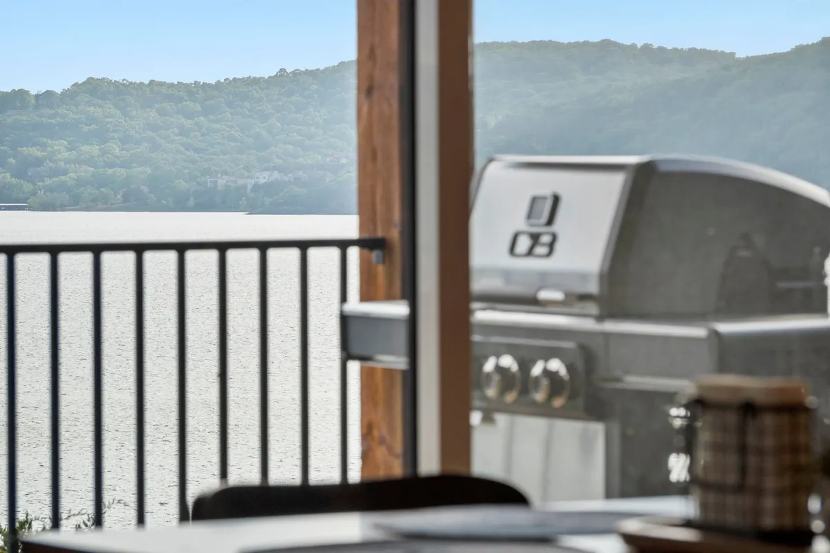 This exterior image features a grill set up next to a breathtaking lake view with a mountainous backdrop. The space is set up for outdoor grilling and relaxing by the water, capturing the essence of leisure and scenic beauty.