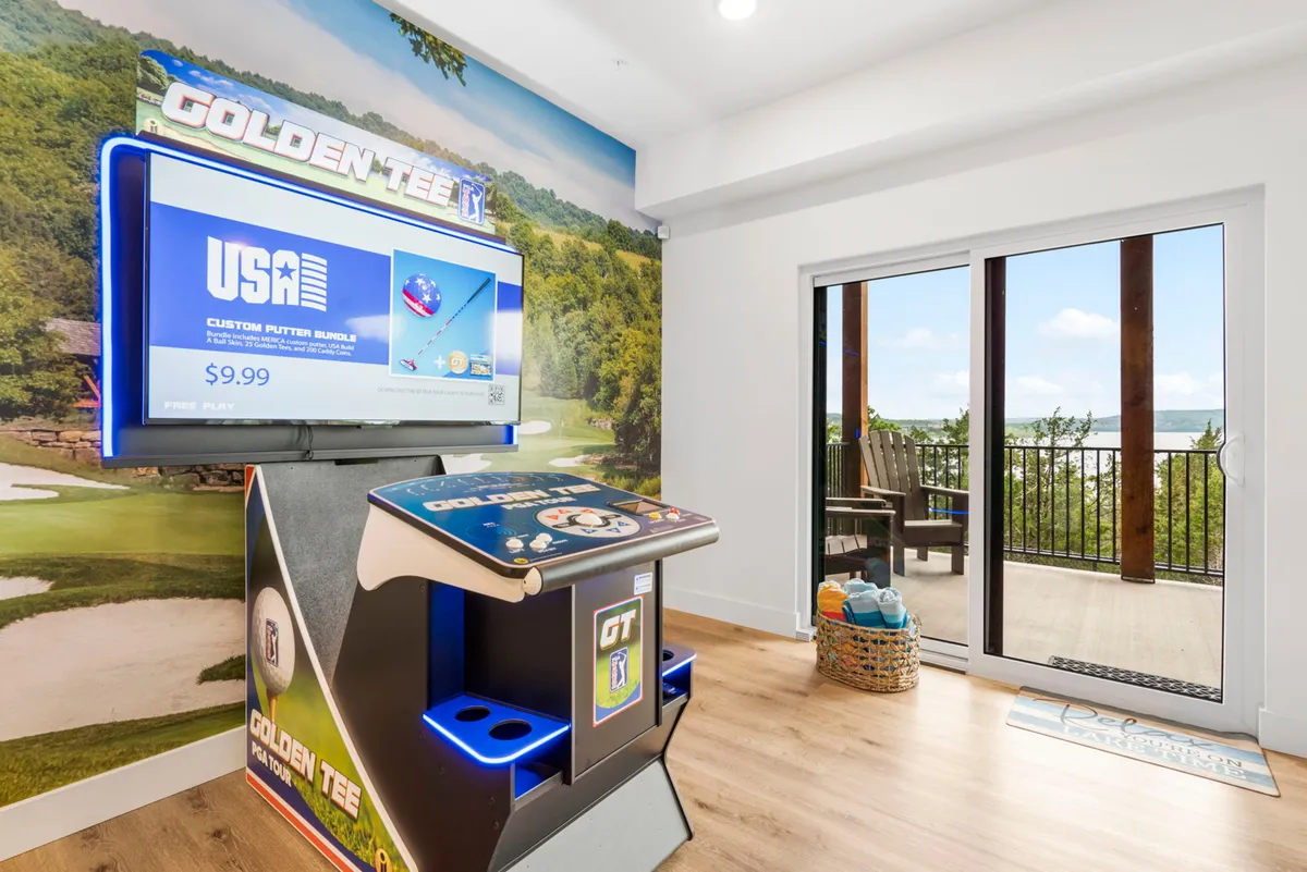 A dedicated game room spotlights a Golden Tee arcade machine, seating, and a balcony view. The setup emphasizes the playful, competitive spirit of arcade gaming and leisure, with natural light streaming in and glimpses of the outdoors.